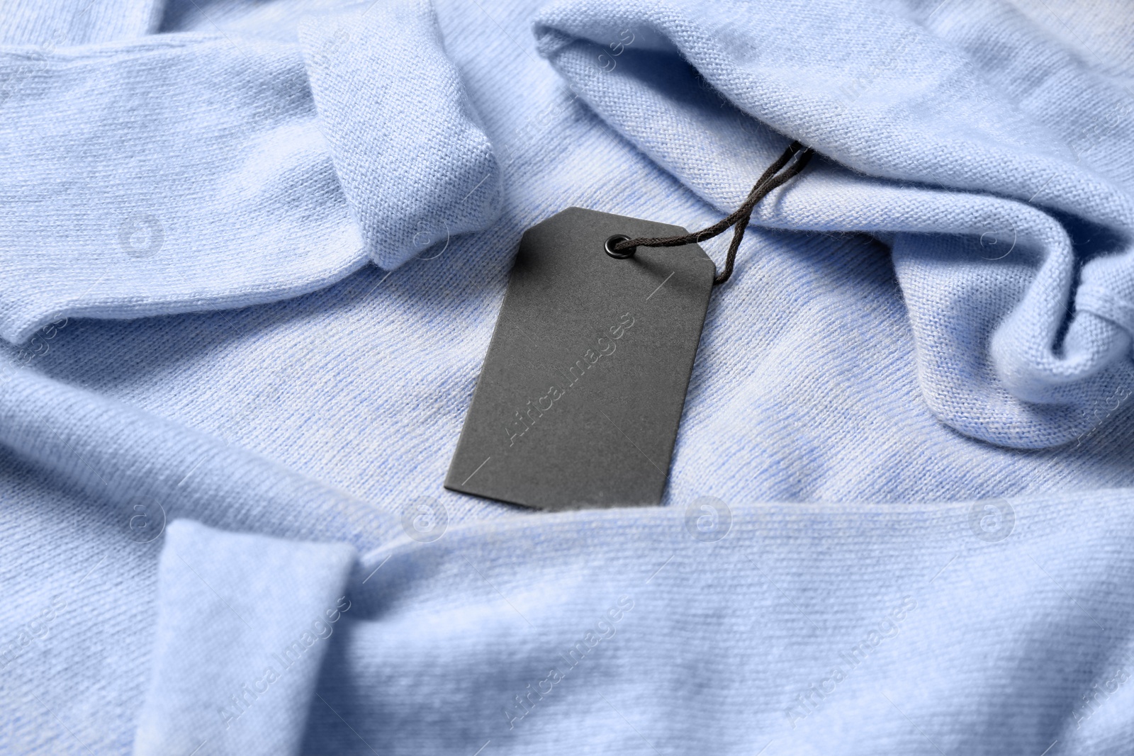 Photo of Blank grey tag on light blue sweater. Space for text