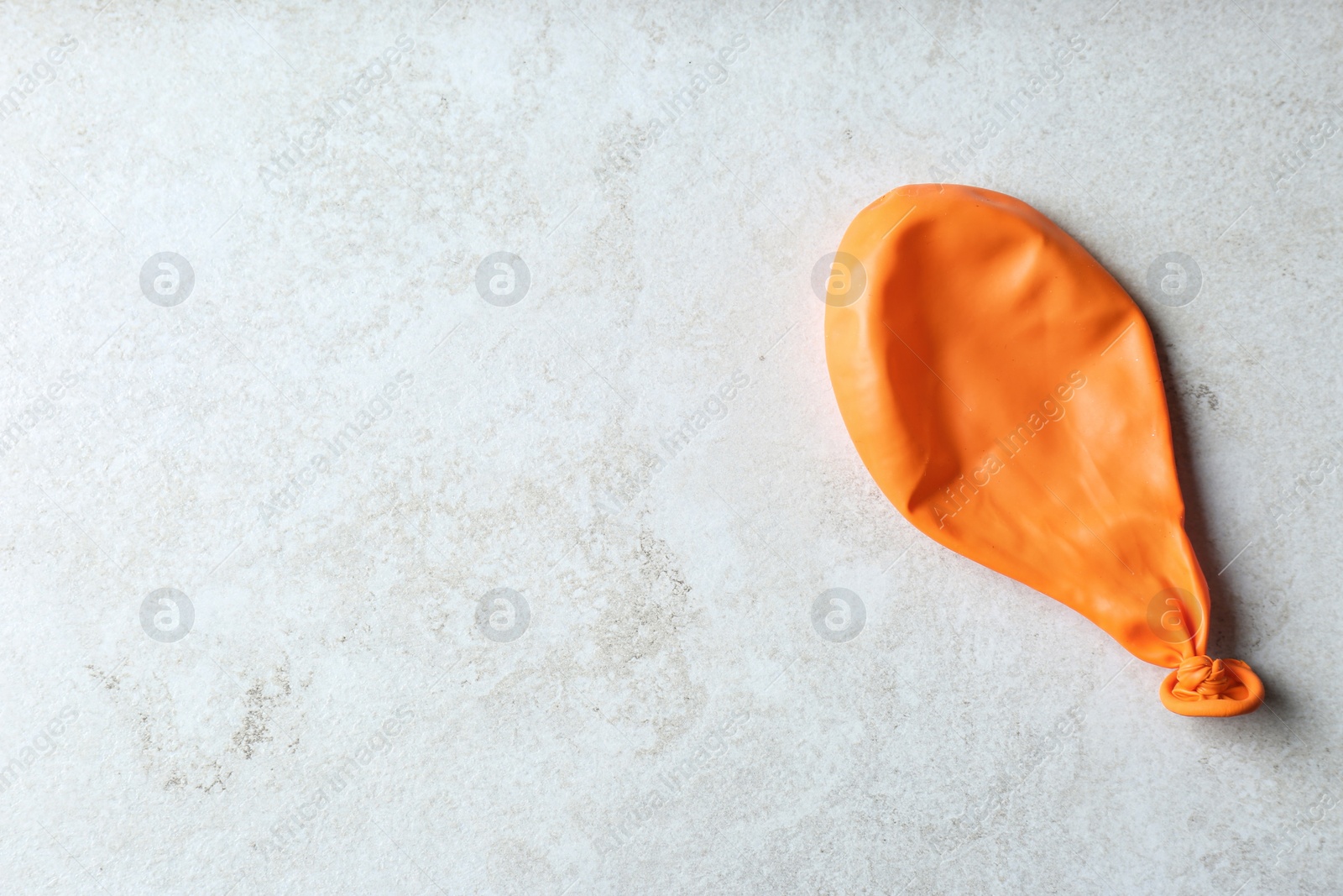 Photo of Orange deflated balloon on grey background, top view with space for text