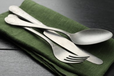 Photo of Stylish setting with cutlery and napkin on black wooden table, closeup