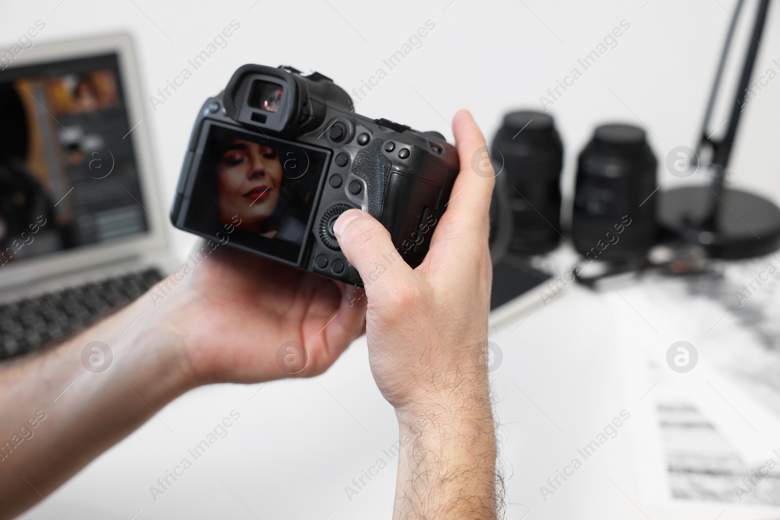 Photo of Professional photographer with digital camera at table indoors, closeup