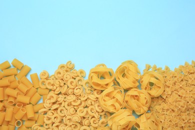 Different types of pasta on light blue background, flat lay. Space for text