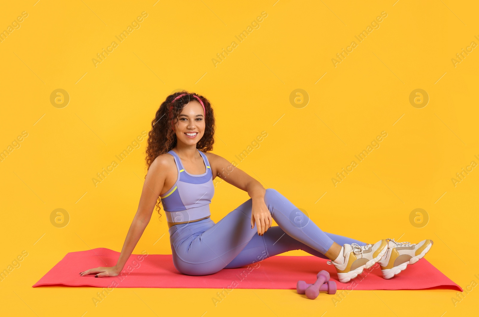 Photo of Beautiful African American woman sitting on yoga mat against yellow background