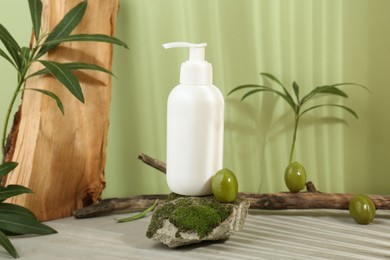 Photo of Bottle of cosmetic product with olive essential oil on stone with moss against light green background