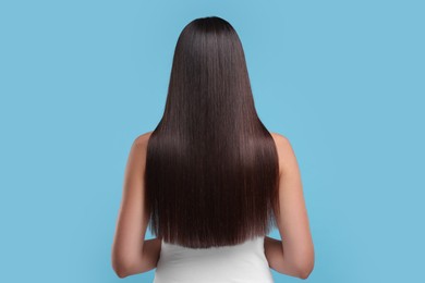 Woman with healthy hair after treatment on light blue background, back view