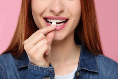 Woman putting bubble gum into mouth on pink background, closeup