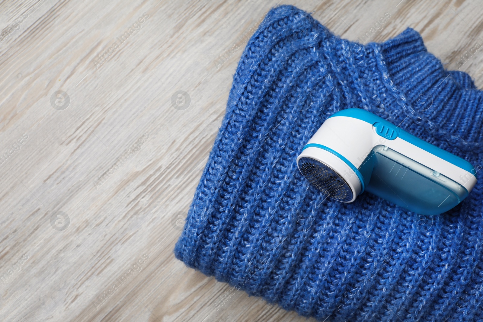 Photo of Modern fabric shaver for lint removing and sweater on wooden table, top view