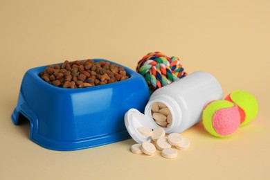 Photo of Bottle with vitamins, toys and dry pet food in bowl on beige background