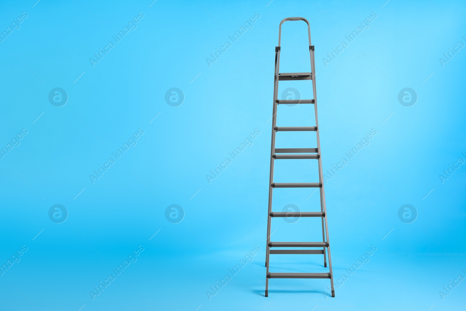 Photo of Metal stepladder on light blue background. Space for text