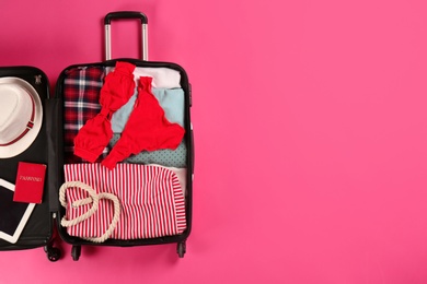 Open suitcase with traveler's belongings on color background, top view. Space for text