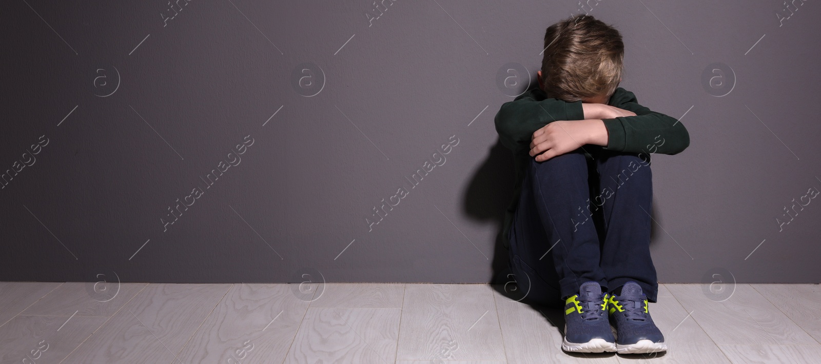 Image of Depressed little boy sitting on floor indoors, banner design with space for text. Time to visit child psychologist