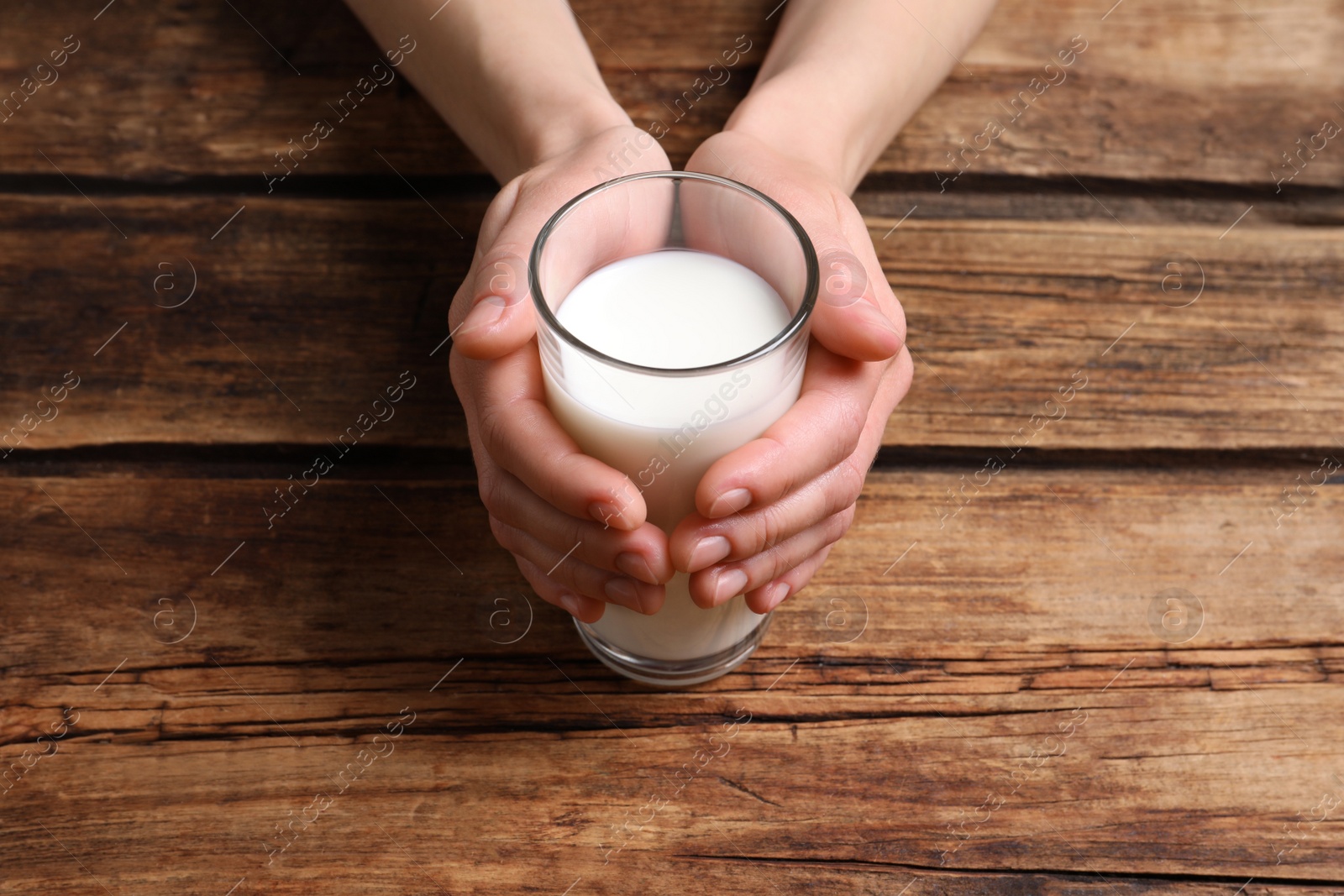 Photo of Woman holding glass of milk at wooden table, closeup