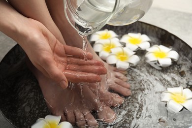 Photo of Woman pouring water onto hand while soaking her feet in bowl, closeup. Spa treatment