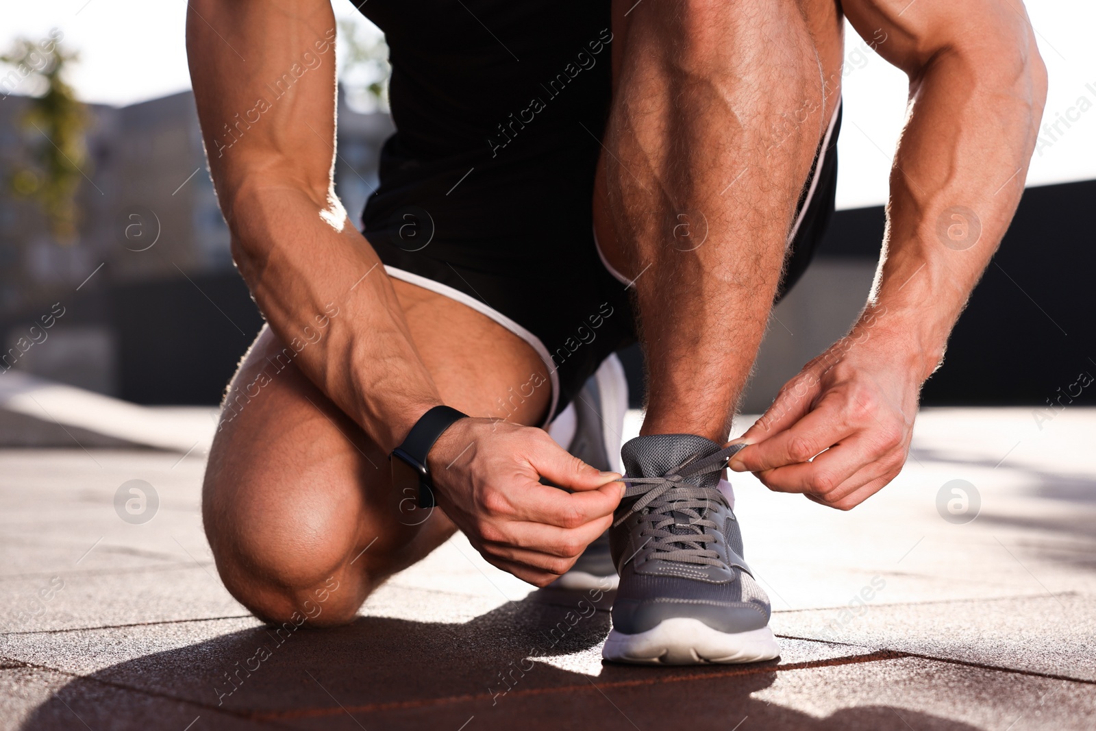 Photo of Man tying shoelaces before running outdoors on sunny day, closeup