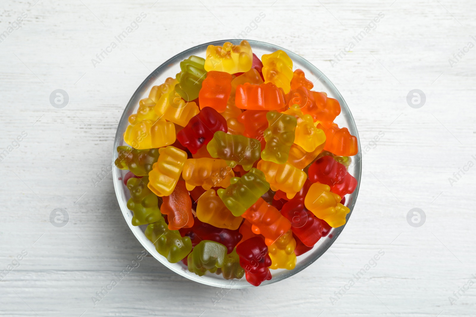 Photo of Bowl with delicious bright jelly bears on white wooden table, top view