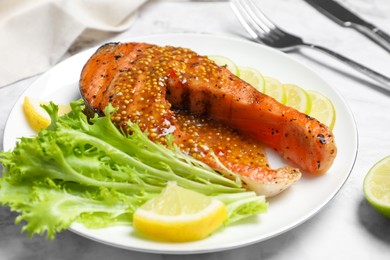 Photo of Tasty salmon steak with sauce, citrus slices and lettuce served on white marble table, closeup