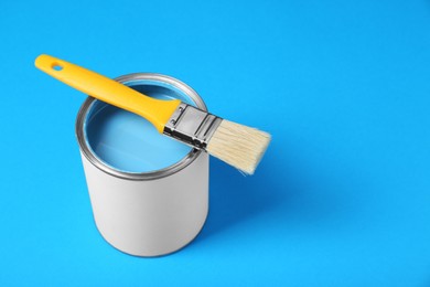 Photo of Can of paint with brush on light blue background, space for text