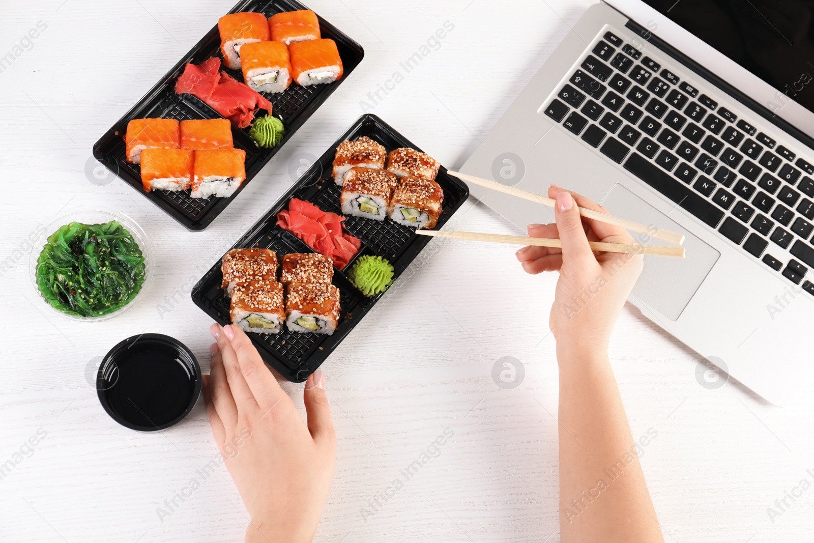 Photo of Woman eating tasty sushi rolls at workplace, closeup. Food delivery