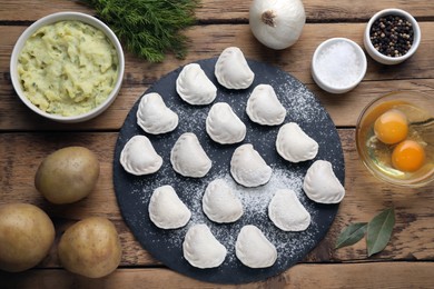 Raw dumplings (varenyky) and ingredients on wooden table, flat lay