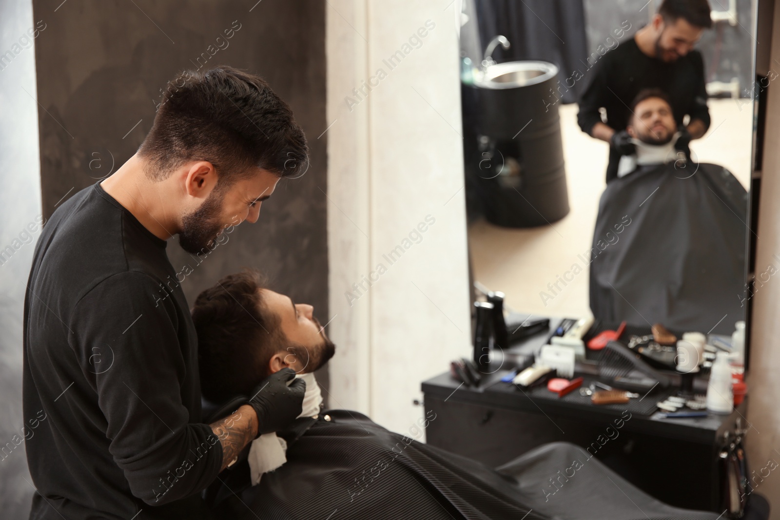 Photo of Professional hairdresser using cold towel to calm client's skin after shaving in barbershop