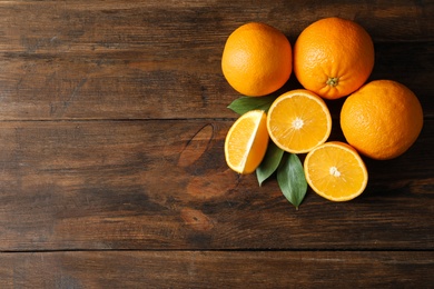 Fresh oranges with leaves on wooden background, top view. Space for text