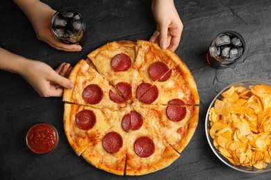 Photo of Women taking tasty pepperoni pizza at grey table, top view