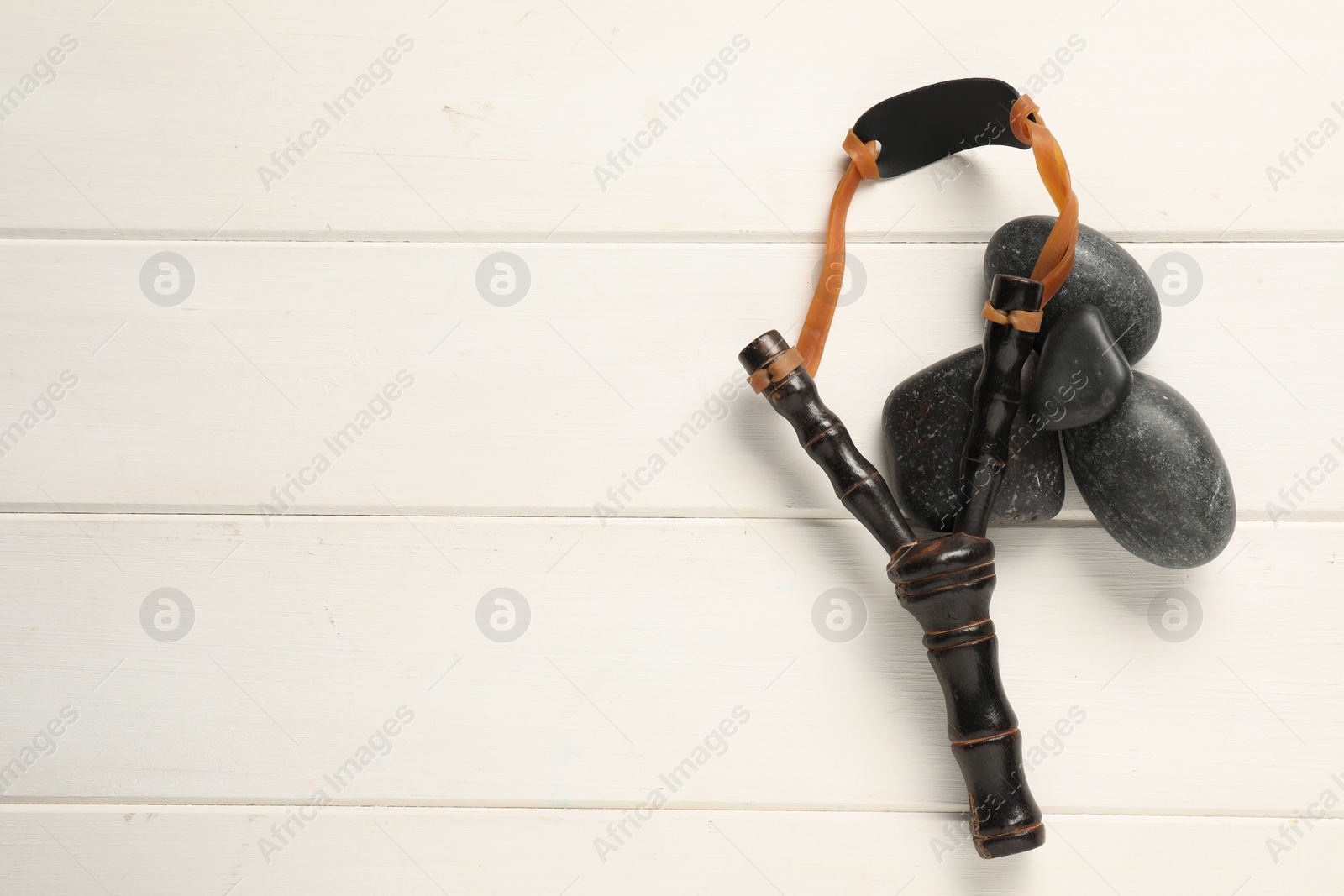 Photo of Black slingshot with stones on white wooden table, flat lay. Space for text