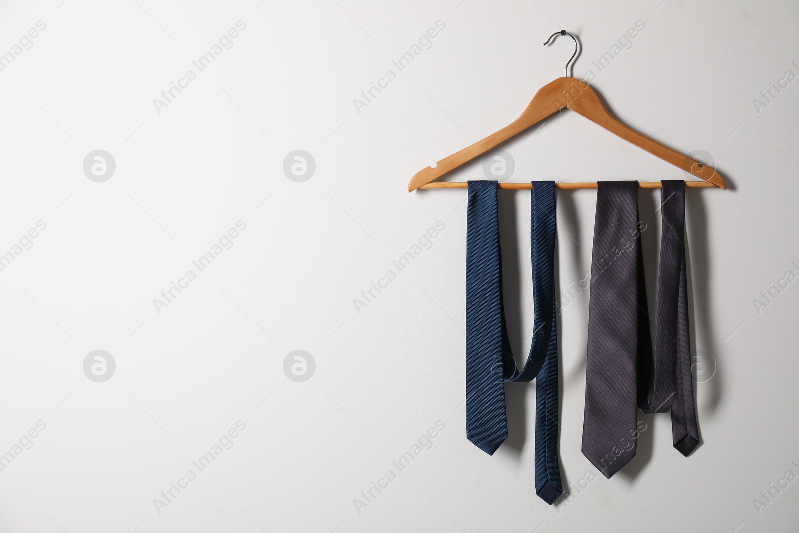 Photo of Hanger with different stylish neckties on light wall. Space for text