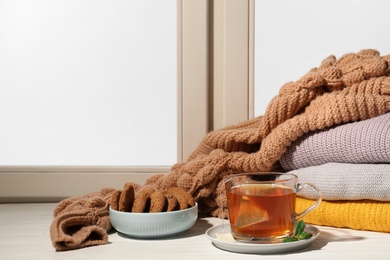 Cup of tea and bowl with cookies on windowsill indoors, space for text. Winter drink