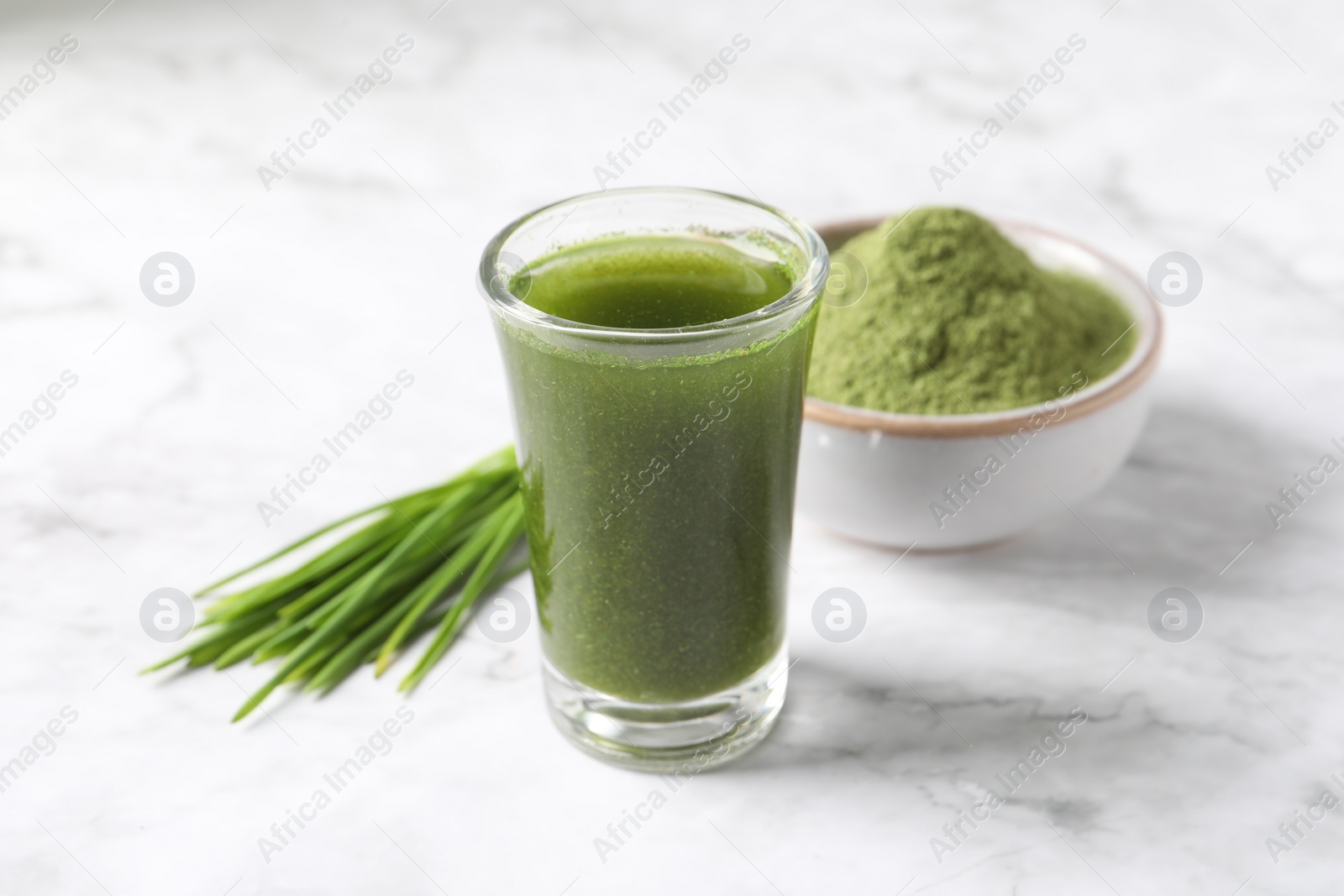 Photo of Wheat grass drink in shot glass on white marble table, closeup