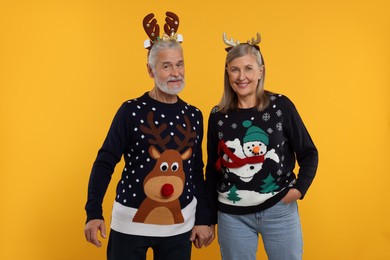 Photo of Senior couple in Christmas sweaters and reindeer headbands on orange background