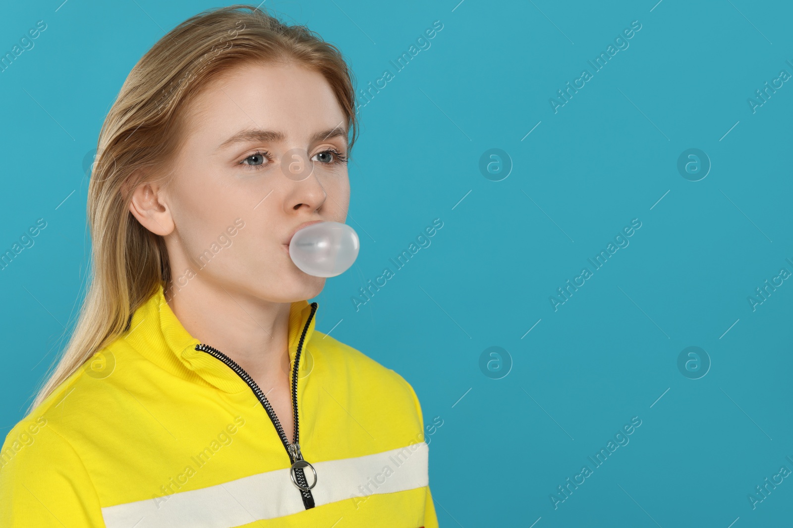 Photo of Beautiful young woman blowing bubble gum on light blue background. Space for text