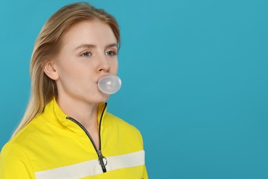 Beautiful young woman blowing bubble gum on light blue background. Space for text