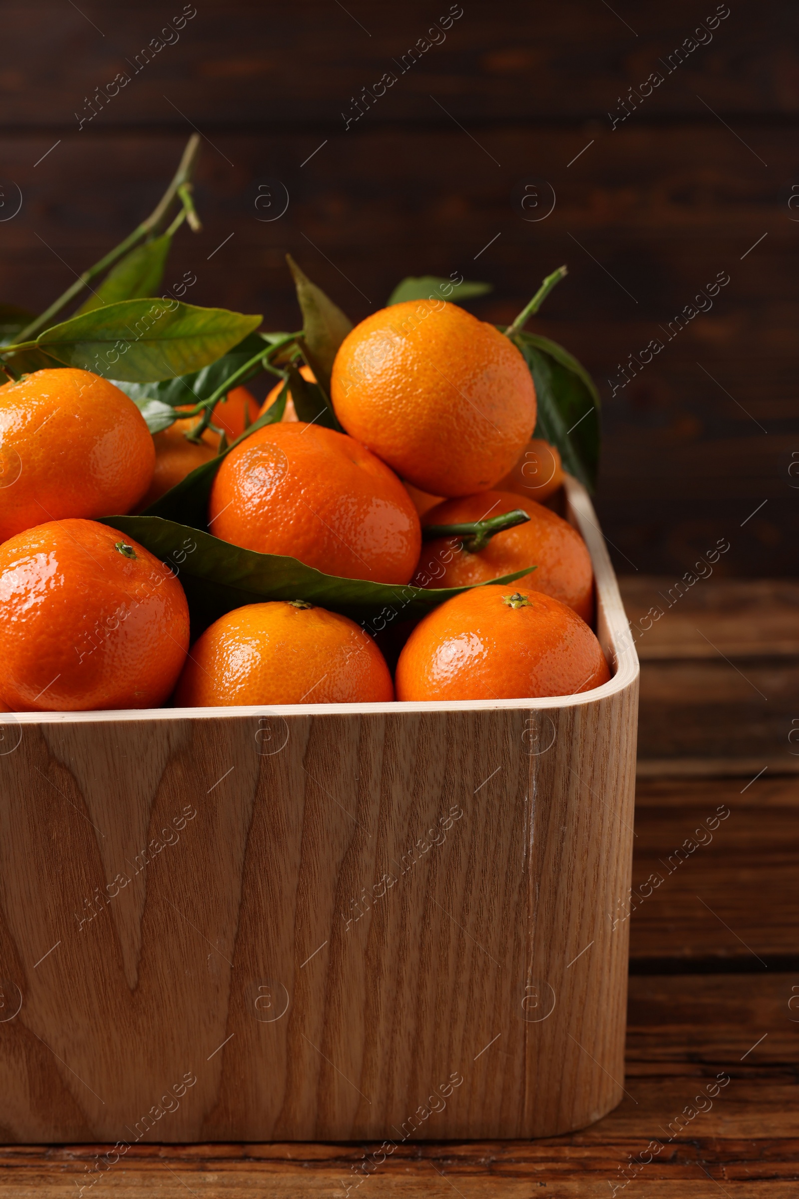 Photo of Fresh tangerines with green leaves in crate on wooden table, closeup