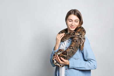 Young woman with boa constrictor on light background, space for text. Exotic pet