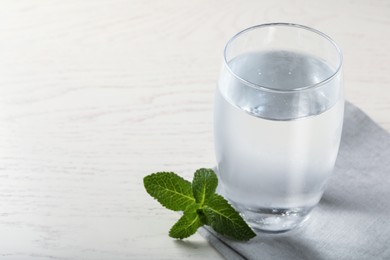 Photo of Glass of soda water, mint and napkin on white wooden table. Space for text