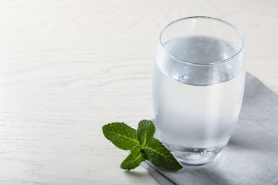 Glass of soda water, mint and napkin on white wooden table. Space for text