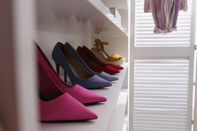 Photo of White shelving unit with collection of colorful high heel shoes indoors. Space for text