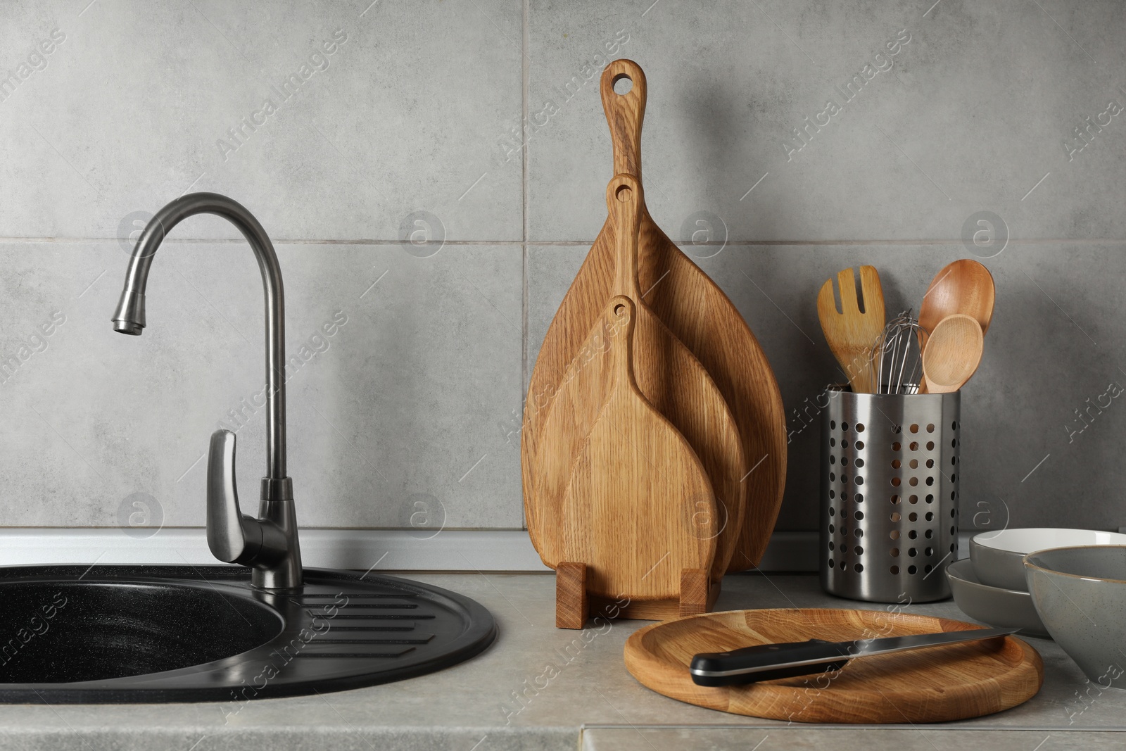 Photo of Wooden cutting boards, other cooking utensils and dishware on light grey countertop in kitchen