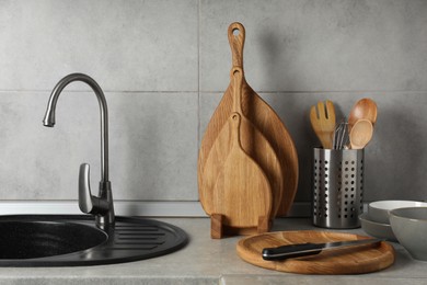 Photo of Wooden cutting boards, other cooking utensils and dishware on light grey countertop in kitchen
