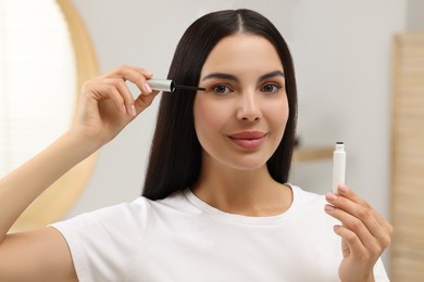 Photo of Beautiful woman applying serum onto her eyelashes indoors. Cosmetic product