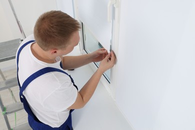 Photo of Worker in uniform installing roller window blind indoors, above view