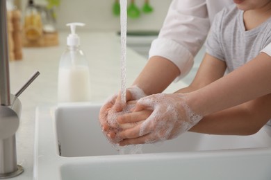 Photo of Mother and daughter washing hands with liquid soap together in kitchen, closeup
