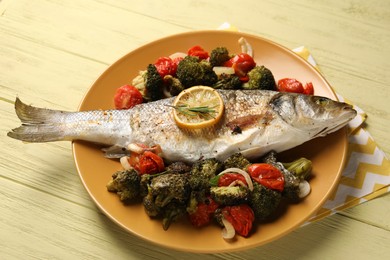 Photo of Delicious baked fish and vegetables on yellow wooden table, above view