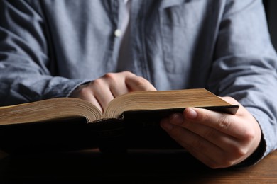 Man reading holy Bible at wooden table, closeup