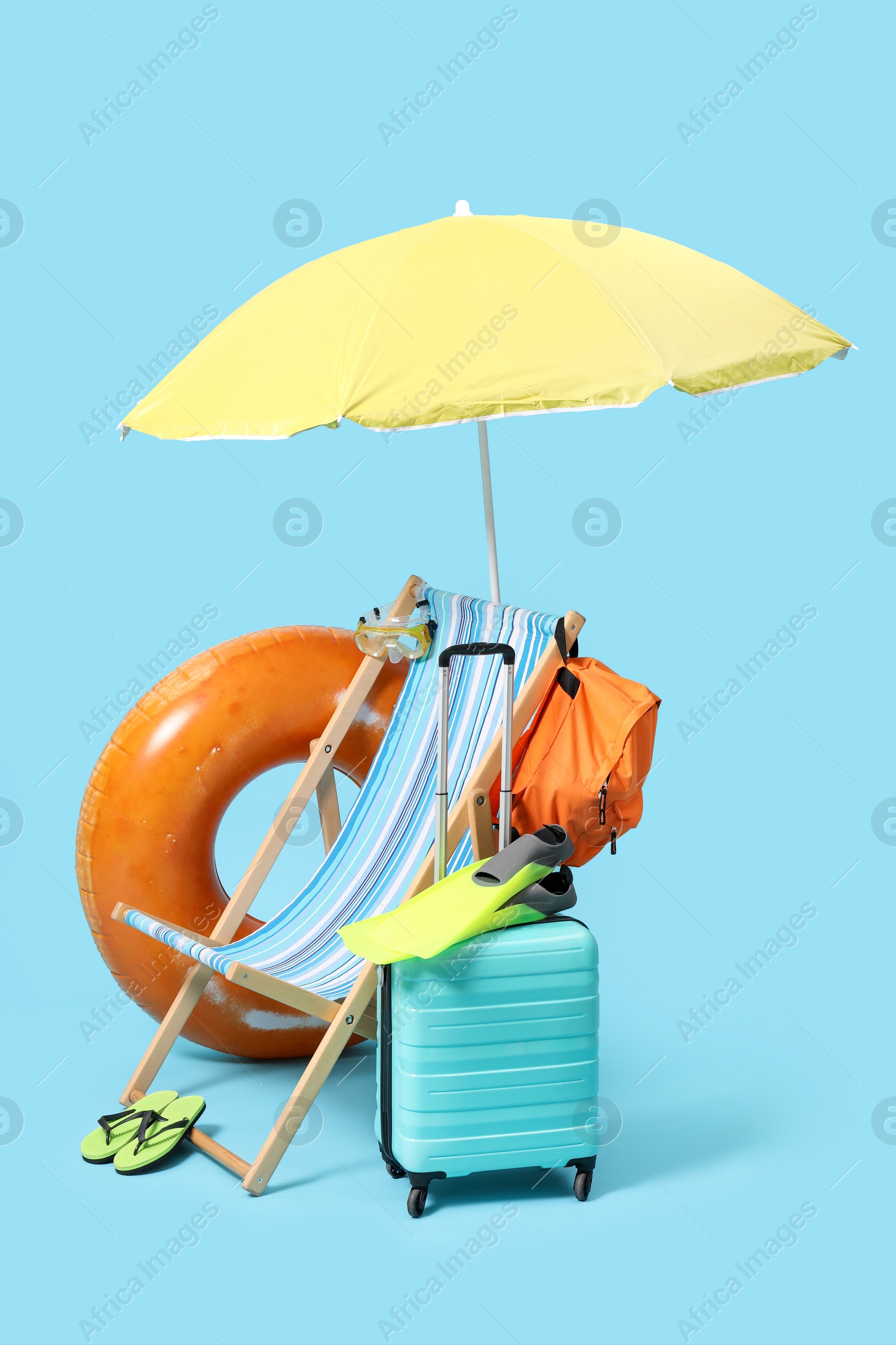 Photo of Deck chair, suitcase, backpack and beach accessories on light blue background