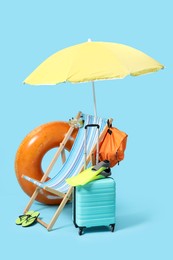 Deck chair, suitcase, backpack and beach accessories on light blue background
