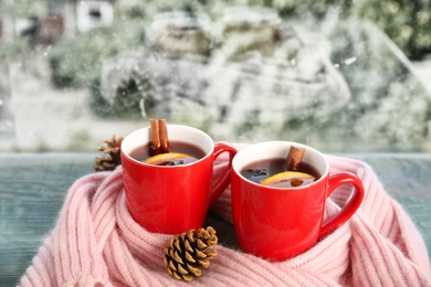 Cups of hot winter drink with scarf on window sill indoors