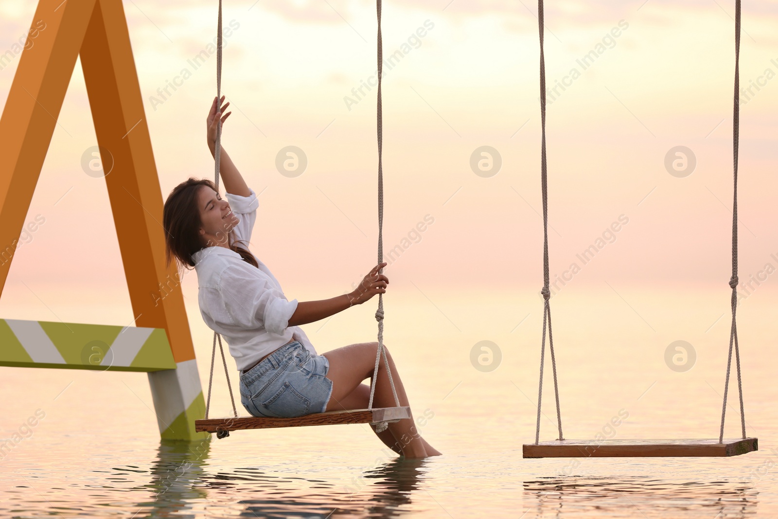 Photo of Young woman enjoying sunrise on swing over water