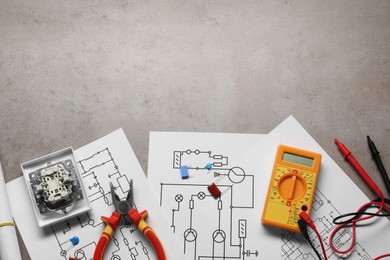 Photo of Wiring diagrams, digital multimeter and other electrician's equipment on grey table, top view. Space for text