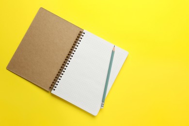 Photo of Notebook and pencil on yellow background, top view. Space for text